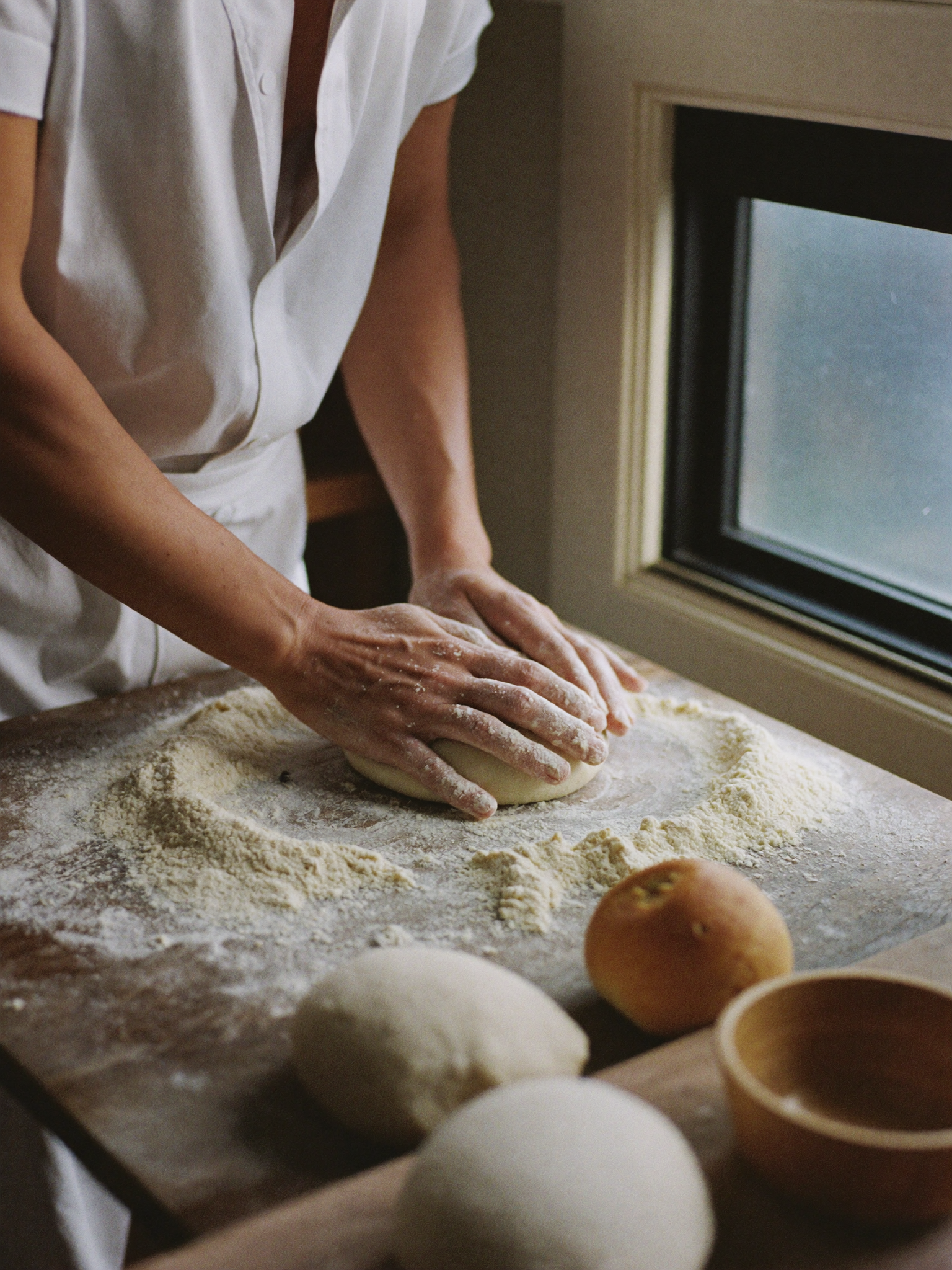 Hands kneading dough on a flour-dusted counter, soft morning light